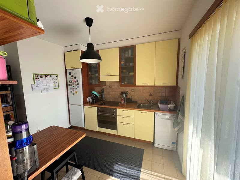 Bright kitchen with light yellow cabinets, white appliances, wooden countertop, and a small dining area with a table and stools.