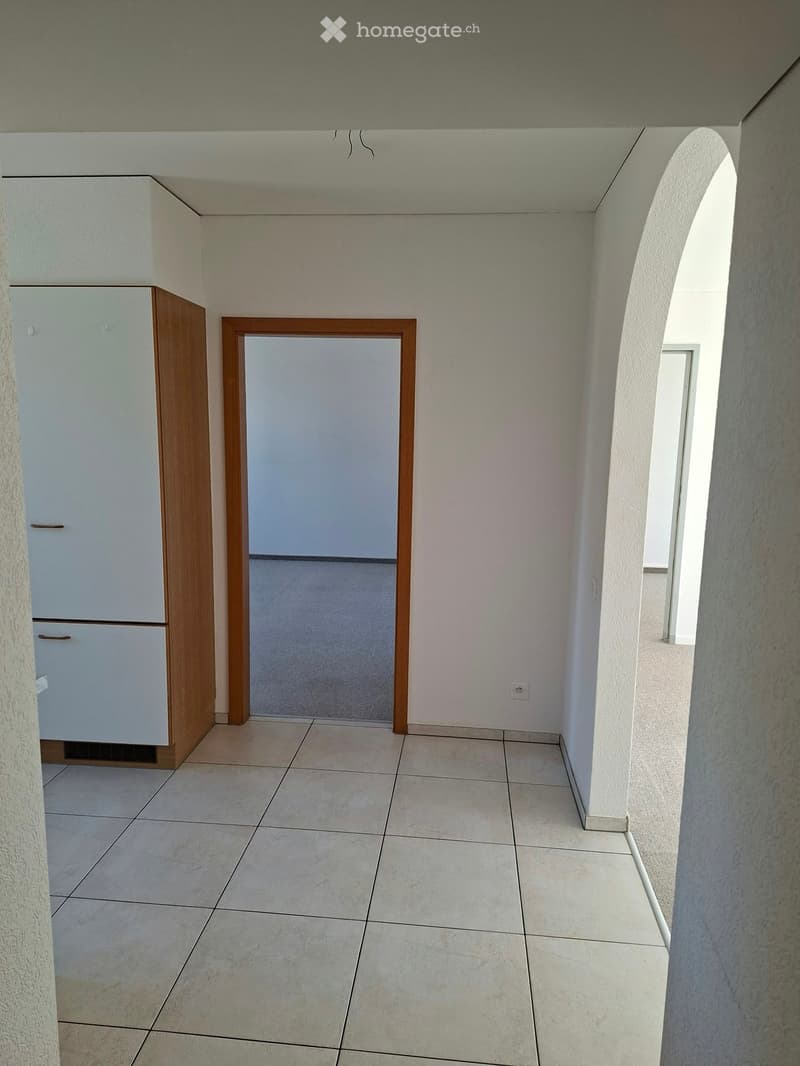 Empty room with tiled floor, white walls, and a wooden cabinet. A doorway leads to another room.