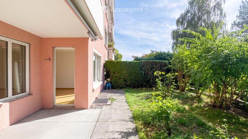 Garden area with a pathway leading to a house entrance, surrounded by greenery and trees.