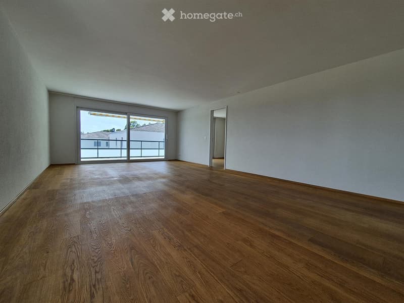 Empty room with wooden flooring, white walls, and large sliding glass doors leading to a balcony.