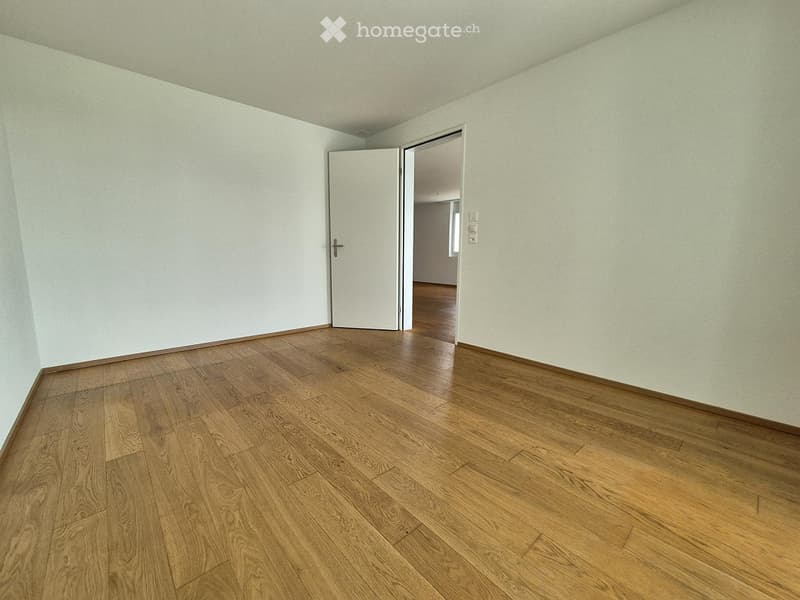 Empty room with light-colored walls and wooden flooring, featuring an open doorway leading to another space.