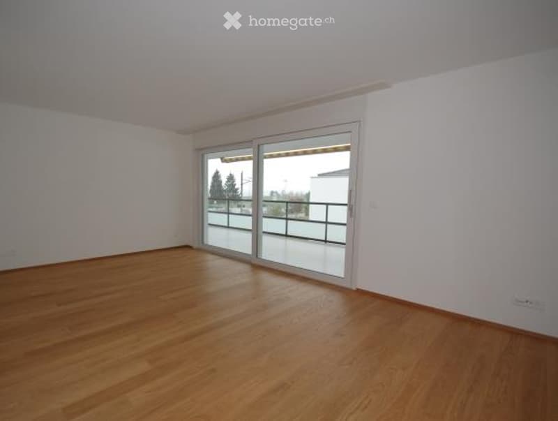Empty room with wooden flooring, white walls, and large sliding glass doors leading to a balcony.