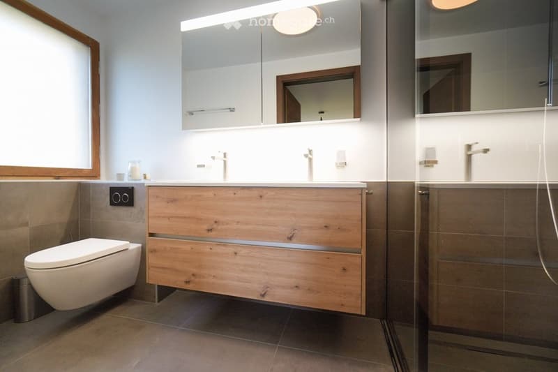 Modern bathroom with a wooden vanity, a toilet, a large mirror, and a glass-enclosed shower area.