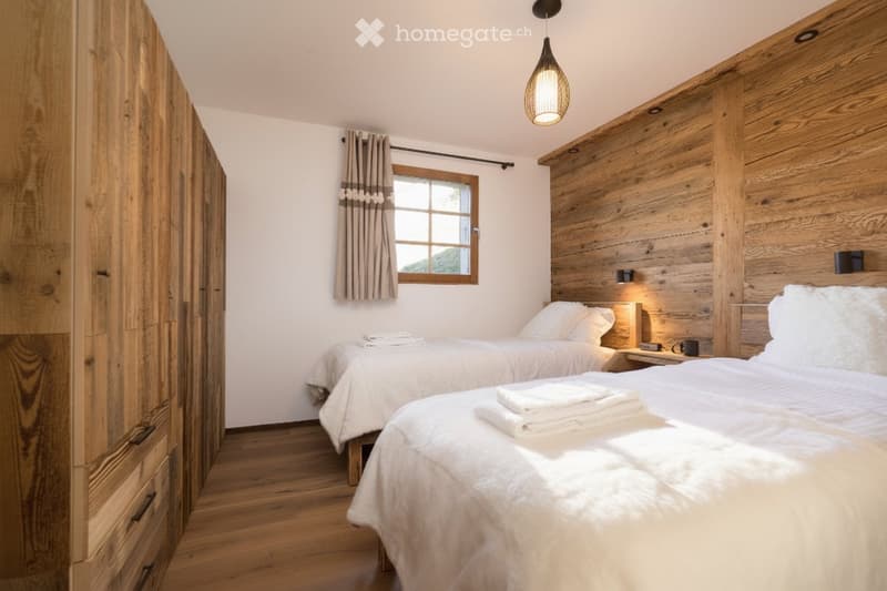 Cozy bedroom with two single beds, wooden walls, nightstand, and a large window with curtains.