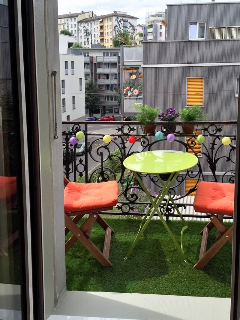 Balcony with green table, orange chairs, small potted plants, and decorative string lights.