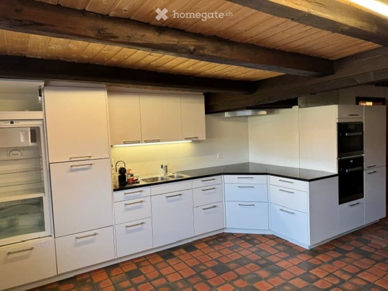 Modern kitchen with white cabinets, stainless steel appliances, and a brick floor. Features include a refrigerator, microwave, oven, sink, and ample cabinet storage.
