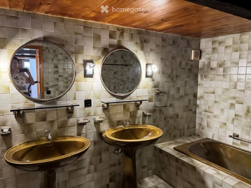 Bathroom with two sinks, mirrors, shelves, and a bathtub, featuring a wooden ceiling and tiled walls.