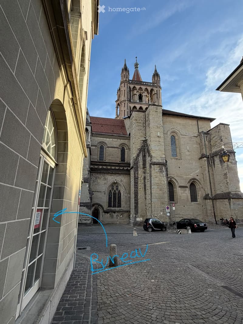 A historic stone church with tall spires and arched windows, situated in a cobblestone courtyard surrounded by modern buildings.