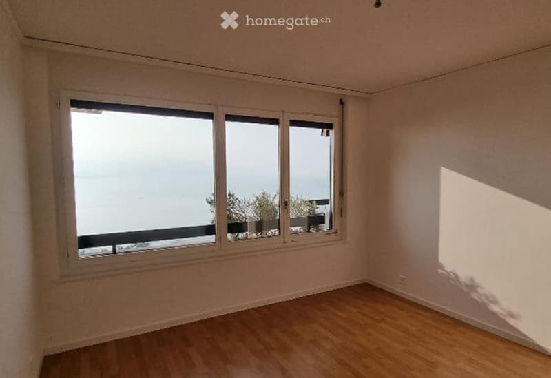 Empty room with wooden flooring and large windows offering a view of the outdoors.