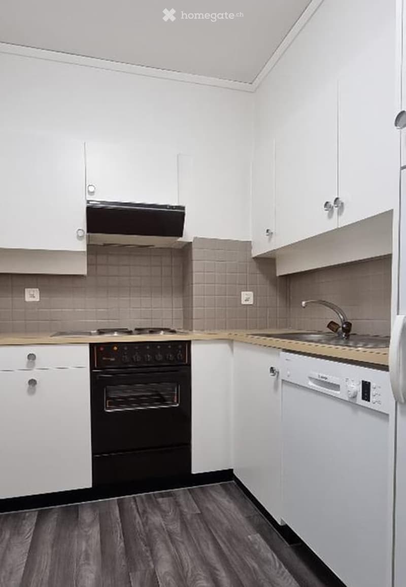 Modern kitchen with white cabinets, black oven, dishwasher, and a sink with a faucet. The countertops are light-colored, and the floor is dark wood.