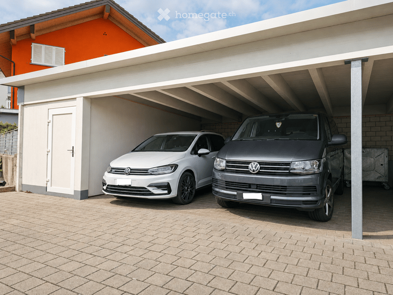 Garage with two parked cars, white and grey, under a covered roof with a brick floor.