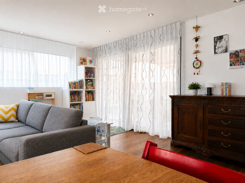 Bright living room with grey sectional sofa, wooden coffee table, red chair, bookshelf, and decorative items.