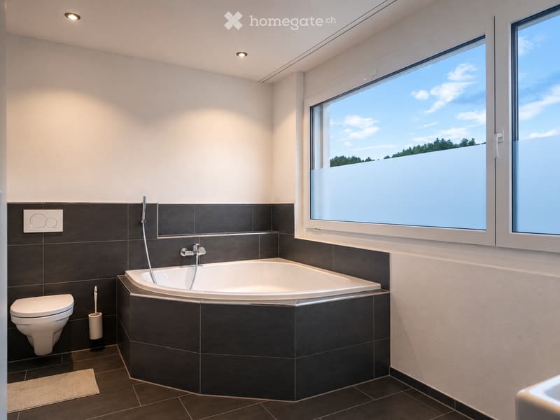 Modern bathroom with a large window offering a scenic view, featuring a bathtub, toilet, and toothbrush holder.