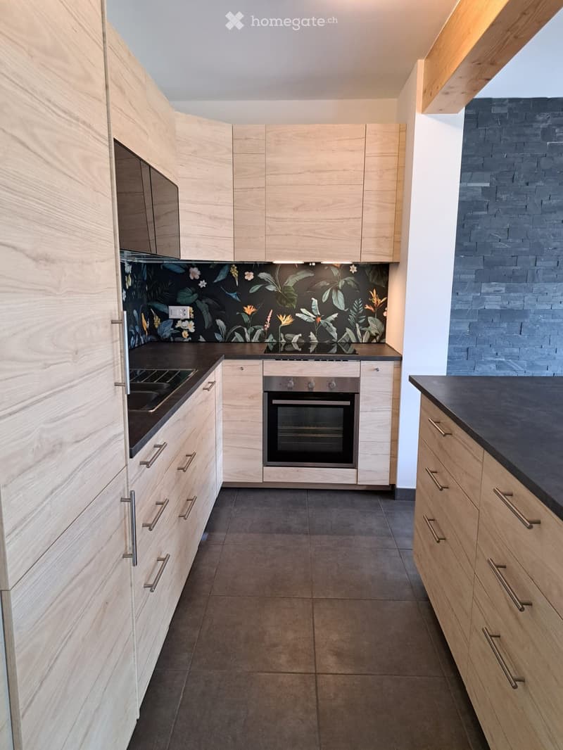 Modern kitchen with light wooden cabinets, stainless steel oven, stove, and dark countertops.
