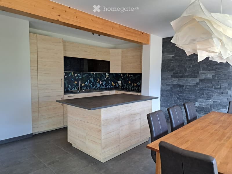 Modern kitchen with light wood cabinetry, a central island, and a dining area with a wooden table and black chairs.