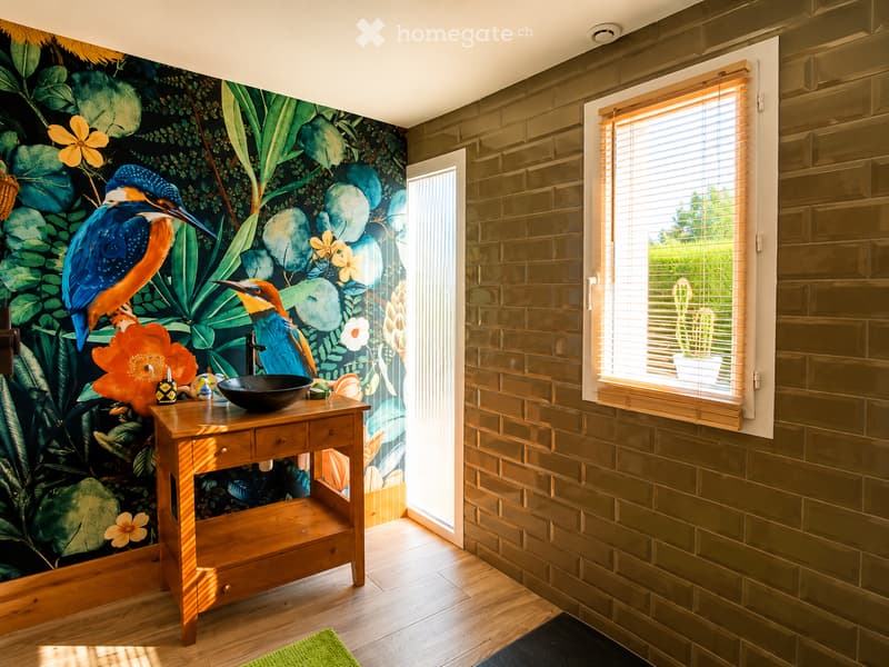 Bathroom with a wooden vanity, black sink bowl, decorative wall mural featuring birds and flowers, and a window with blinds.
