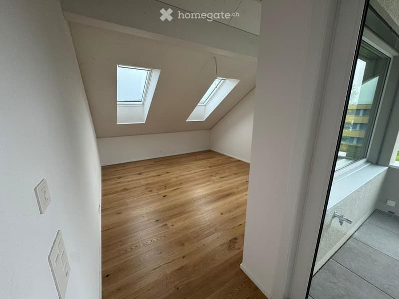 Empty attic room with wooden flooring, white walls, and skylight windows. No furniture or equipment present.