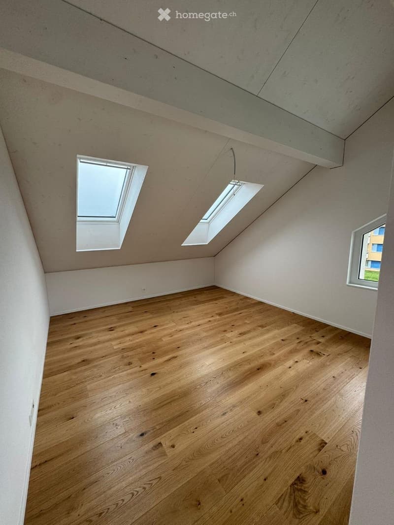 Empty attic or loft space with wooden flooring, exposed concrete ceiling, and skylight windows providing natural light.