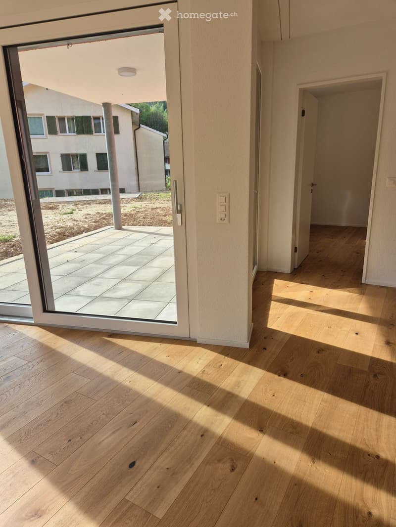 Bright hallway with light wooden flooring, large sliding glass door leading to a patio area, and a view of a neighboring building.