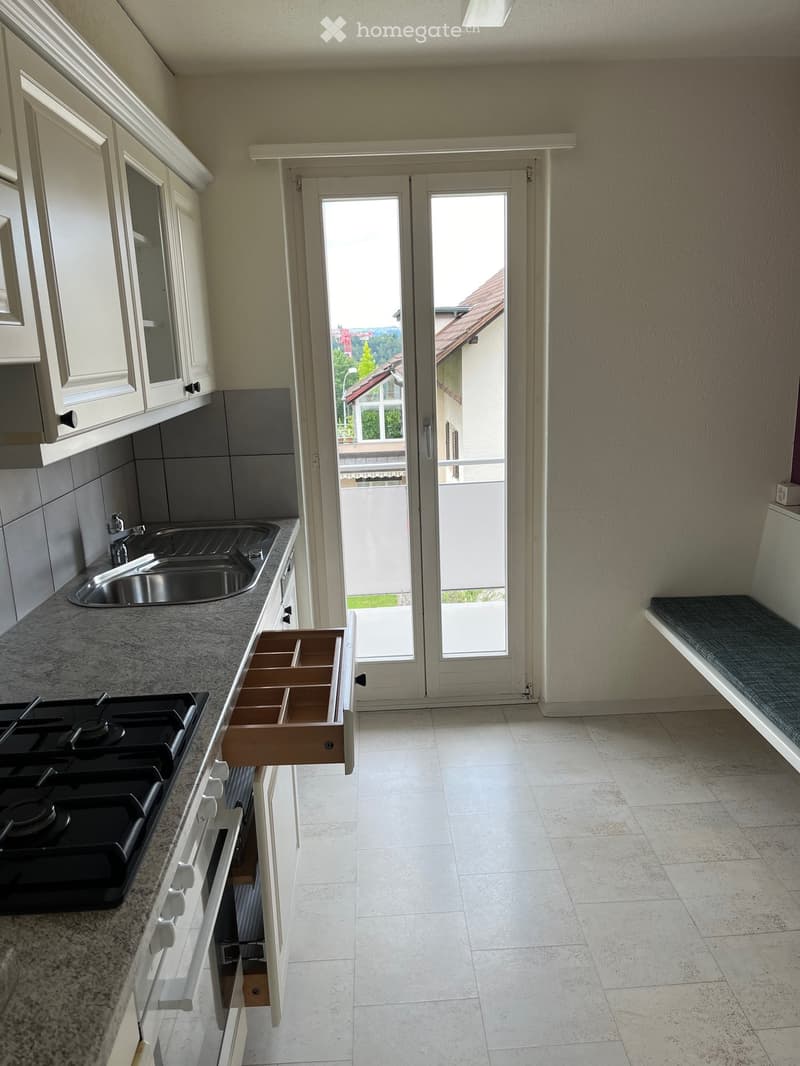 Modern kitchen with white cabinets, granite countertop, gas stove, sink, and an open drawer. Large sliding glass door leads to a balcony.