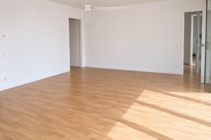 Empty room with light wooden flooring and white walls, featuring two doors and electrical outlets.