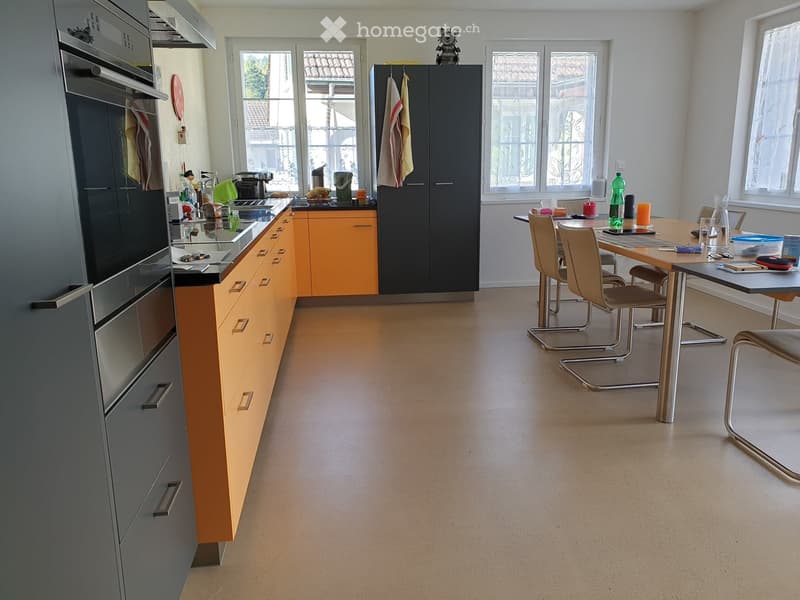 Modern kitchen with orange and grey cabinets, stainless steel appliances, a central island, and a dining area with a table and chairs.