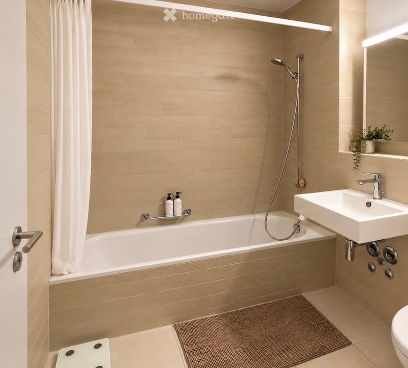 Modern bathroom with beige tiles, a bathtub, a sink, a showerhead, a bathroom rug, and a small plant on the shelf.