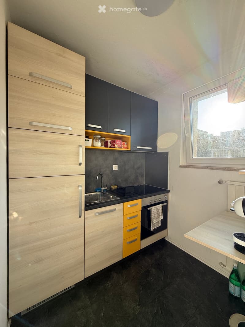 Modern kitchen with light wood cabinets, dark countertops, sink, oven, and various appliances.