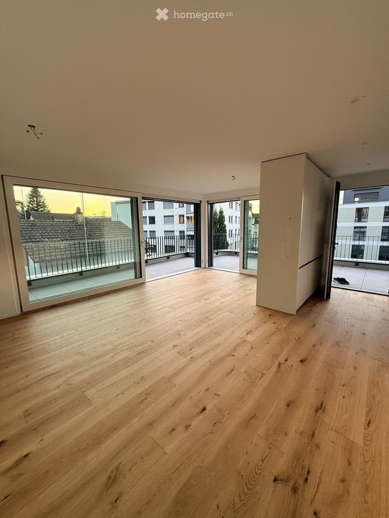 Empty room with light wooden flooring and large glass sliding doors leading to a balcony area.