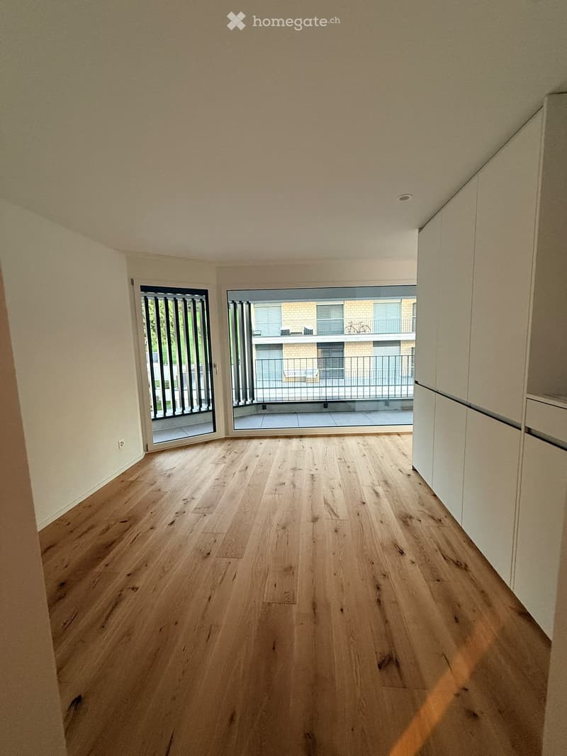 Empty room with light wooden flooring, white walls, and large sliding glass doors leading to a balcony.