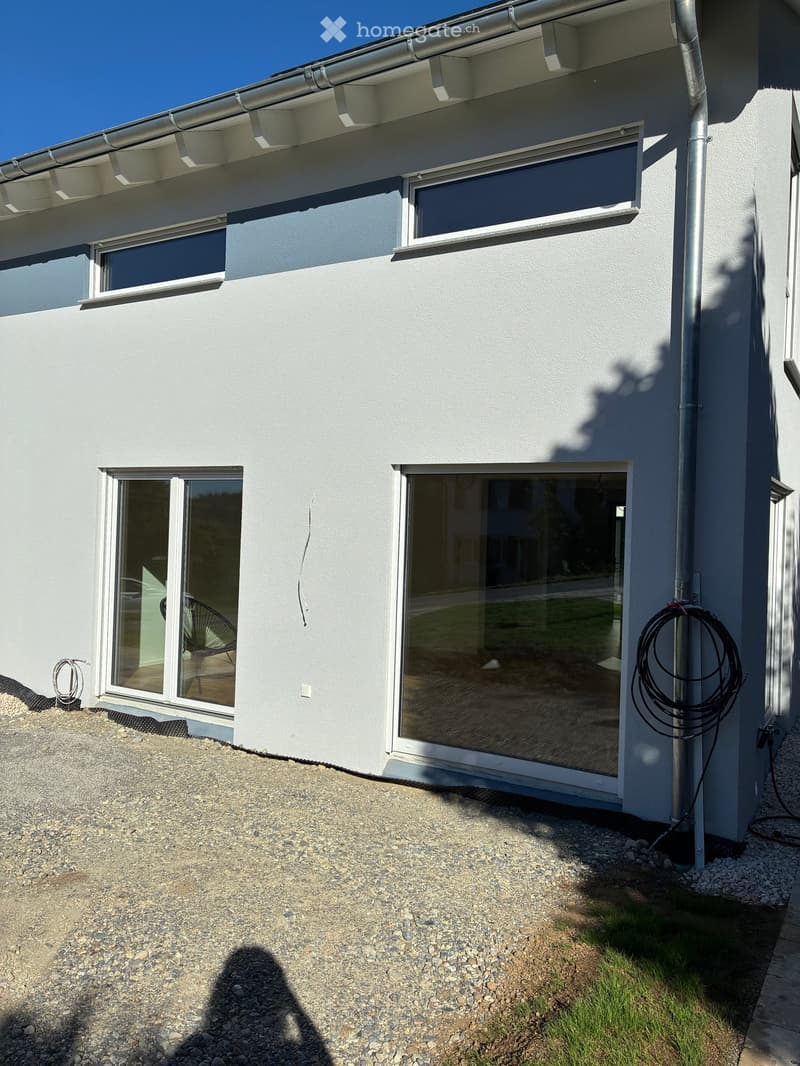 Modern single-story house with white exterior, large windows, and a raised ground floor area with gravel and grass.