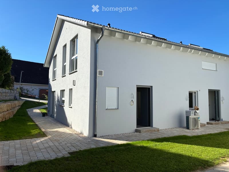 Modern single-story house with white exterior, multiple windows, and a paved pathway leading to the entrance.
