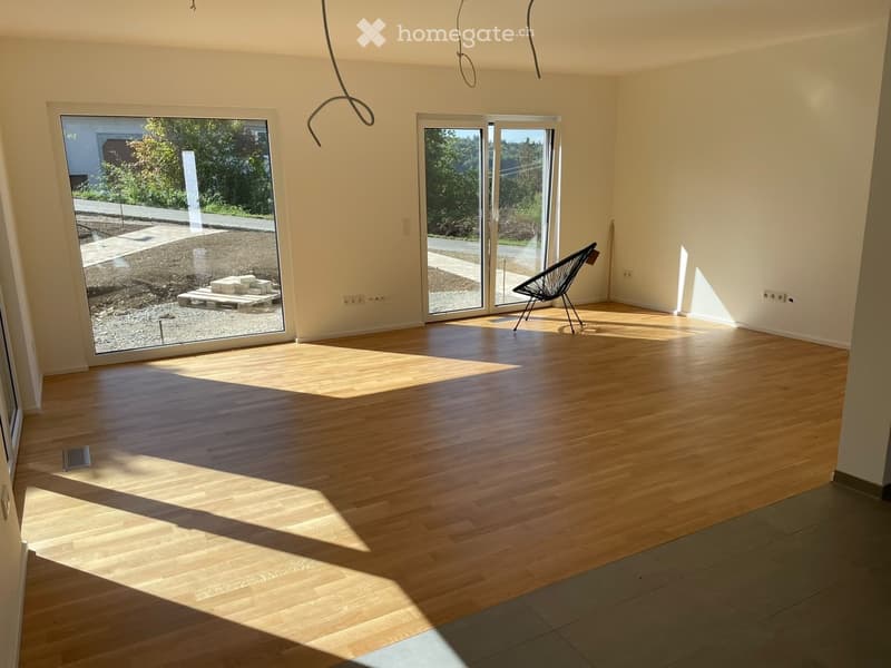 Empty room with wooden flooring, large windows, and a single modern chair near the sliding doors.