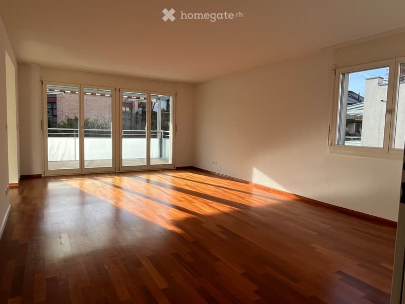 Empty room with wooden flooring, large windows, and sliding glass doors leading to a balcony.