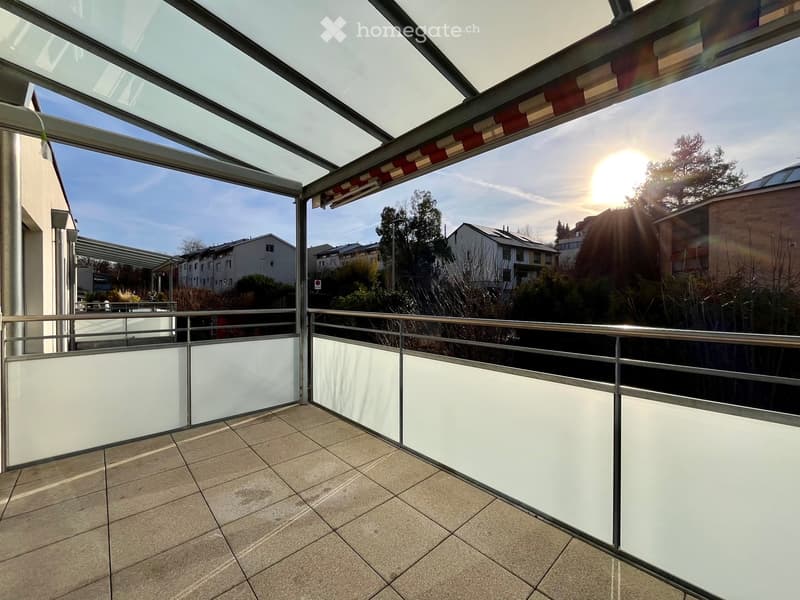 Balcony with tiled floor, metal railing, and a retractable awning, overlooking a residential area with houses and trees.