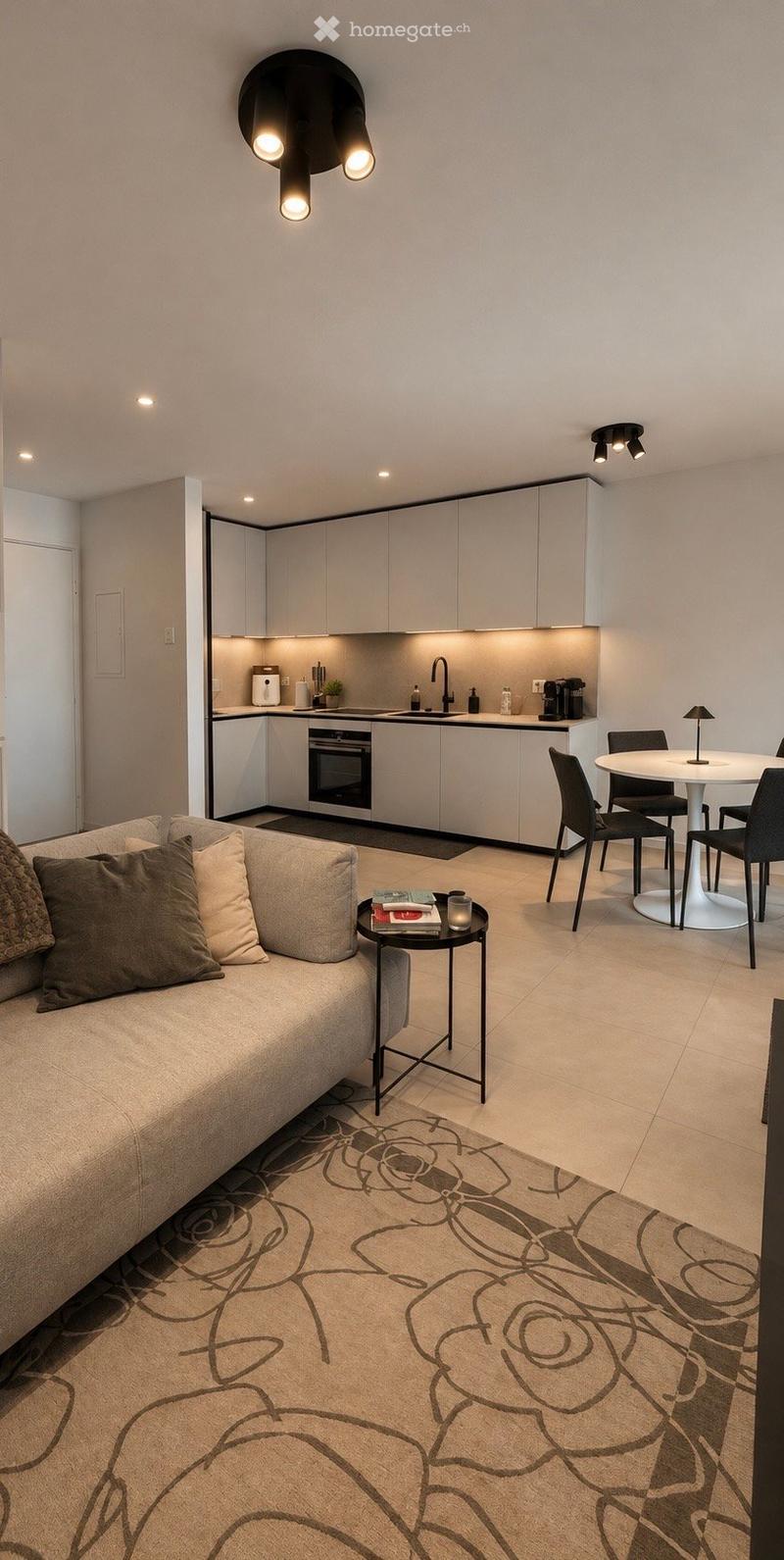 Modern open-plan living and dining area with a sofa, coffee table, dining table, chairs, and a compact kitchen featuring white cabinets, an oven, and a sink.