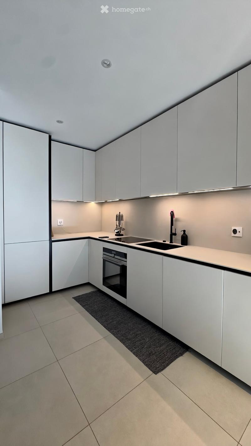 Modern kitchen with white cabinets, a sink, an oven, and a small black rug on the floor.