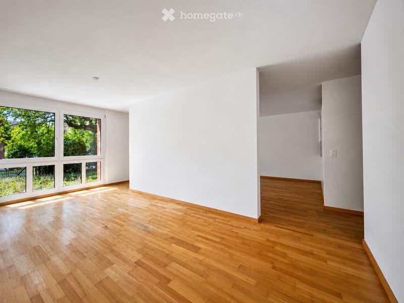 Empty room with light wooden flooring and white walls, featuring large windows that let in natural light.