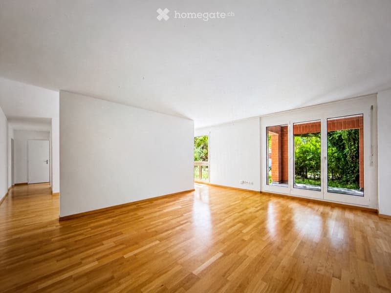 Empty room with light wooden flooring, white walls, and large windows with sliding glass doors leading to a balcony.