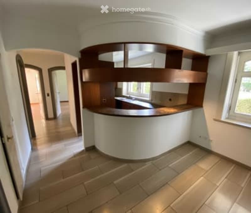 Modern kitchen with a white island, built-in wooden cabinets, and a sink. The space features light wooden flooring and large windows allowing natural light.