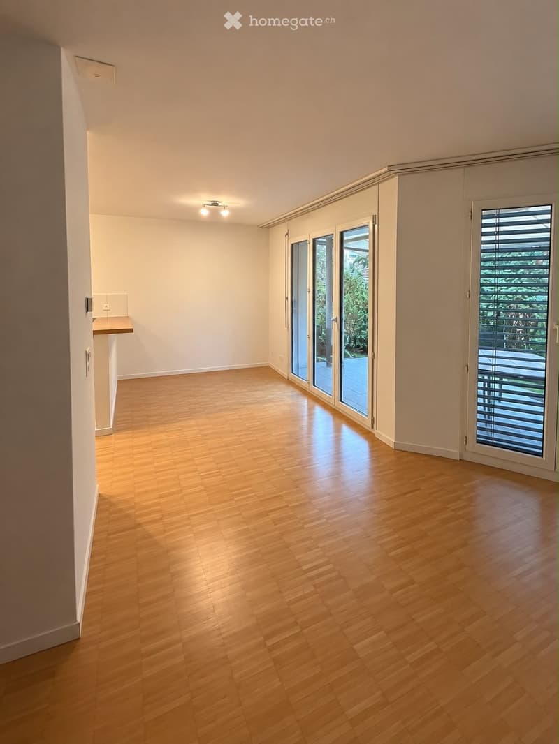 Empty room with light wooden flooring, white walls, and large sliding glass doors leading to an outdoor area.