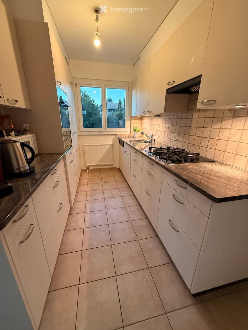 Modern kitchen with white cabinets, tiled floor, gas stove, sink, and various appliances.