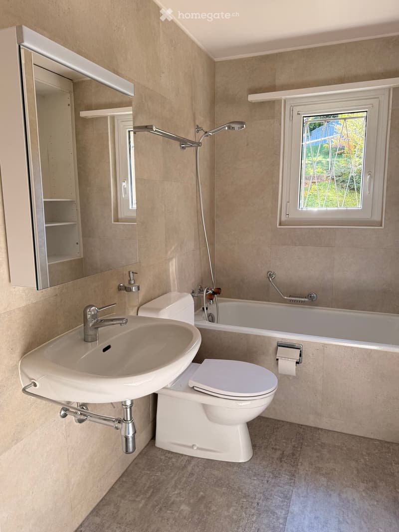 Modern bathroom with beige tiled walls, a white sink, toilet, bathtub, and a large mirror with built-in cabinetry.