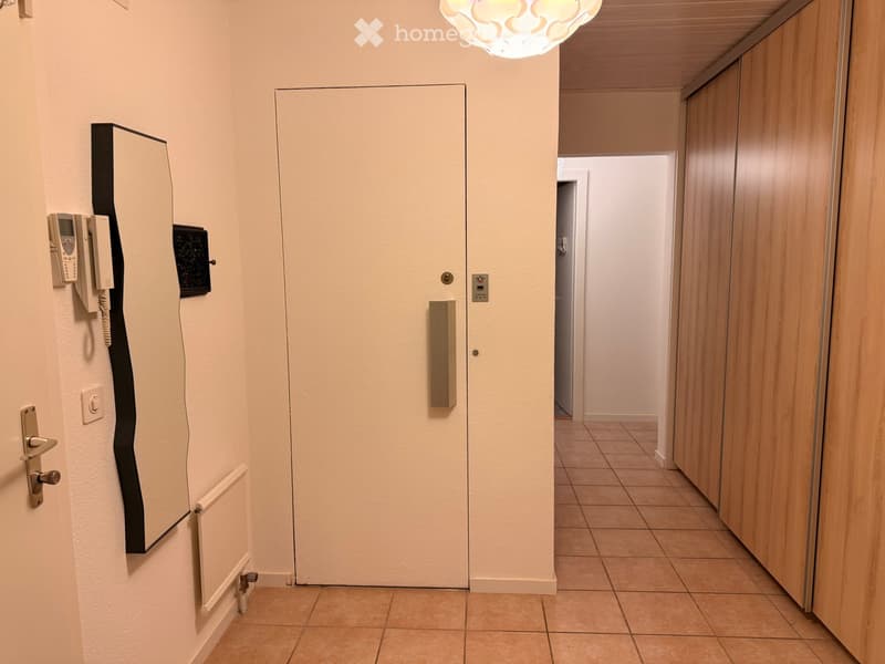 Empty hallway with tiled floor, wooden paneling on one side, and a closed door at the end.