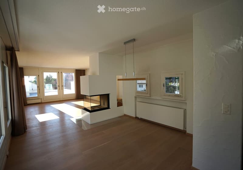 Empty living room with wooden flooring, fireplace, large windows, and sliding glass doors leading to a balcony.
