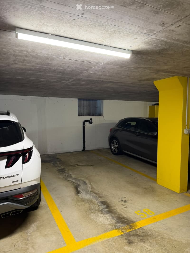 Underground parking space with two cars parked, concrete floor, yellow painted lines, and a yellow pillar.