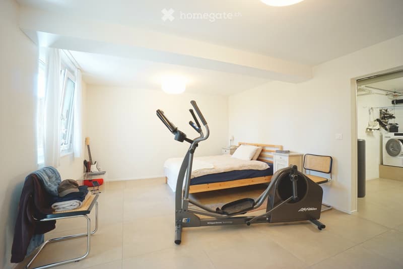 Well-lit room with a bed, elliptical trainer, guitar, chair, washing machine, nightstand, and mirror.