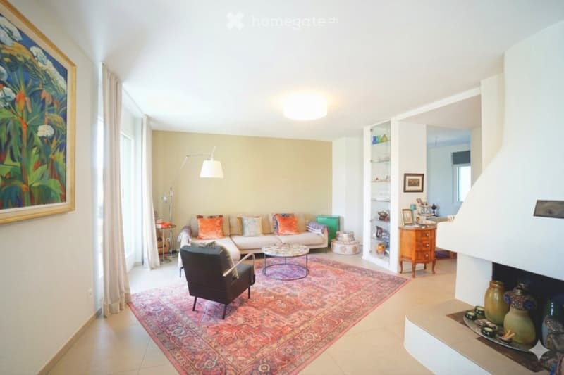 Modern living room with a white sofa, colorful cushions, a coffee table, an armchair, a floor lamp, and a large area rug.