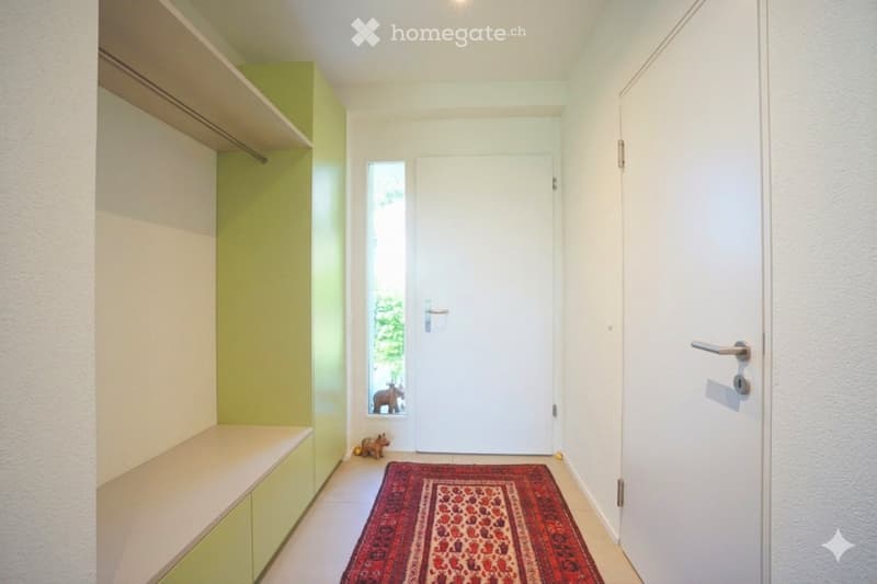 A modern hallway with a built-in bench, a red patterned rug, and a small decorative statue near the door.