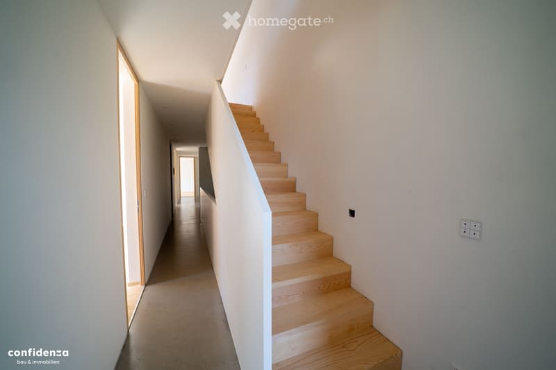 Modern hallway with a wooden staircase leading upwards, white walls, and a light-colored floor.